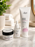 Three Lumo skincare products arranged on a marble surface: a brightening cream jar with a black lid, a small serum dropper bottle, and a larger vitamin C face wash tube, with folded towels and a plant in the softly lit background.